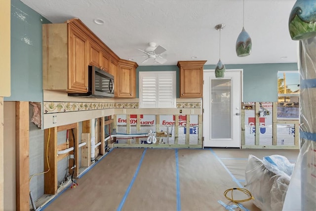 kitchen with brown cabinetry, a ceiling fan, stainless steel microwave, hanging light fixtures, and a textured ceiling