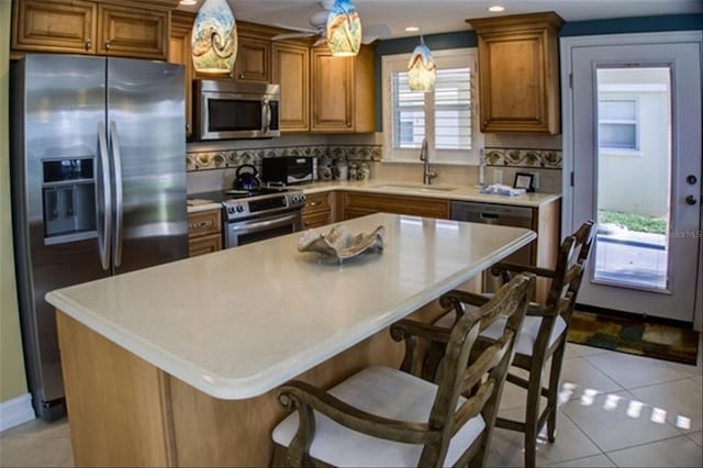 kitchen with a breakfast bar, pendant lighting, light countertops, appliances with stainless steel finishes, and a sink