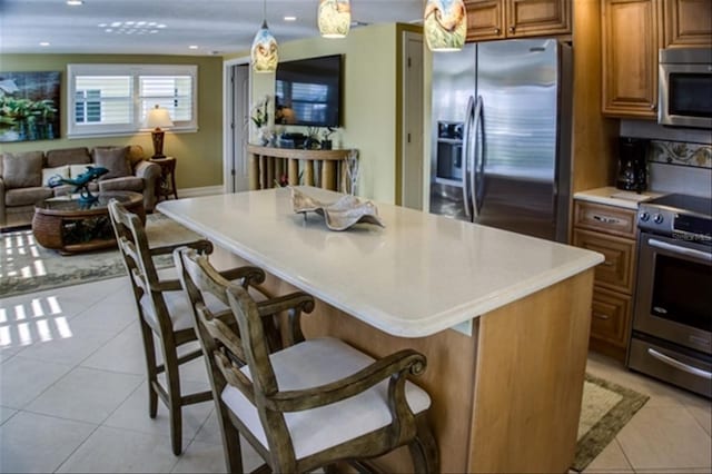 kitchen featuring appliances with stainless steel finishes, light countertops, hanging light fixtures, and a kitchen breakfast bar