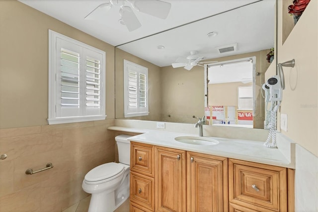 bathroom featuring tile walls, visible vents, toilet, ceiling fan, and vanity