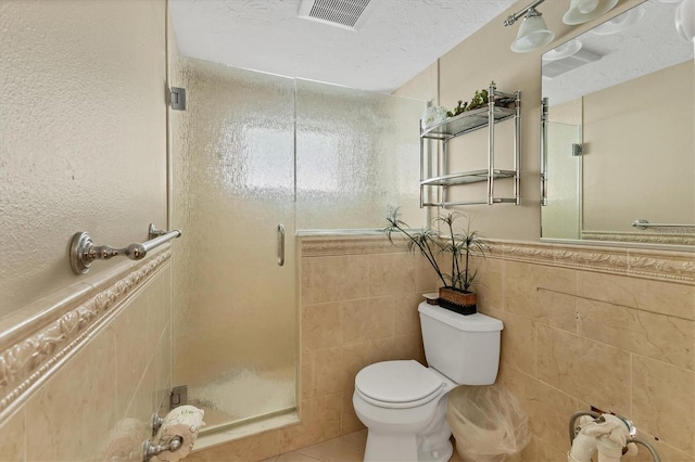 full bathroom featuring tile walls, visible vents, toilet, a shower stall, and a textured ceiling