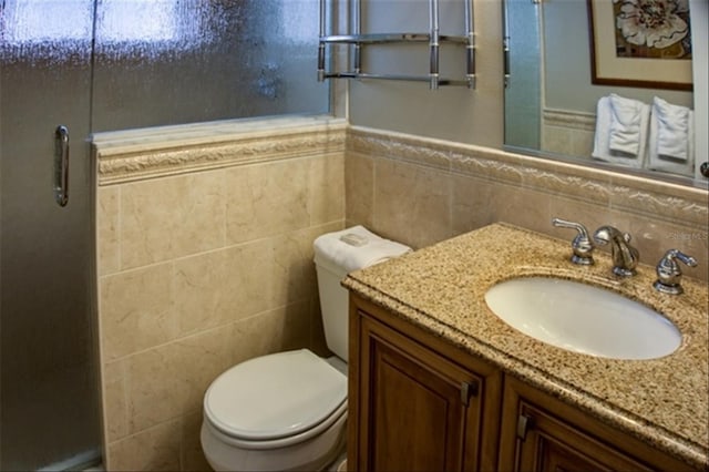 bathroom with toilet, wainscoting, tile walls, and vanity