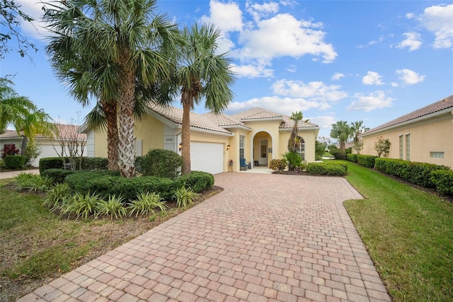 mediterranean / spanish house featuring an attached garage, a tiled roof, decorative driveway, stucco siding, and a front yard