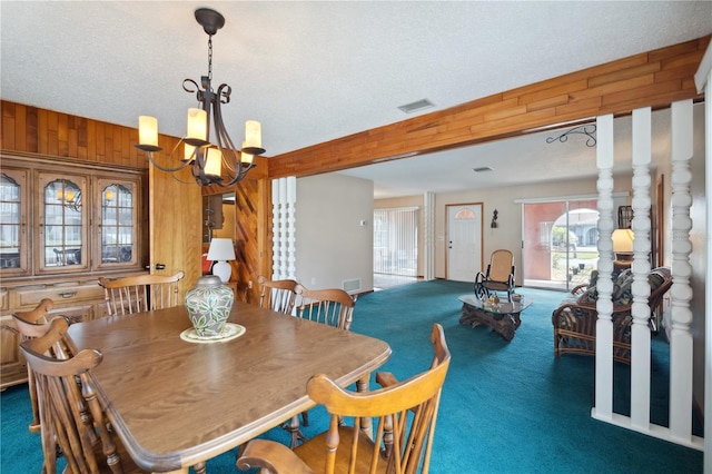 dining space with wood walls, visible vents, dark carpet, and an inviting chandelier