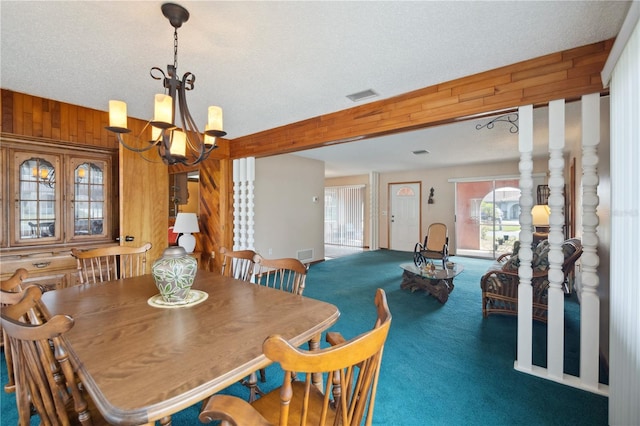 carpeted dining room featuring a chandelier, a textured ceiling, visible vents, and wooden walls