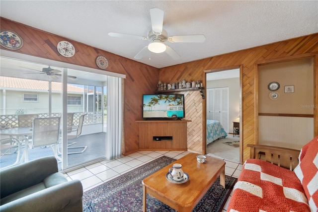 living area with light tile patterned floors, a textured ceiling, wooden walls, a fireplace, and a ceiling fan