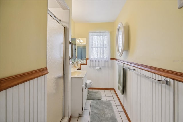 full bath featuring wainscoting, toilet, tile patterned floors, vanity, and a shower stall