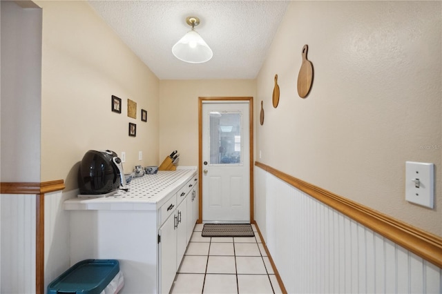 entryway with wainscoting, light tile patterned flooring, and a textured ceiling