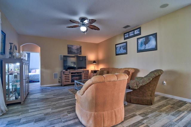 living area featuring arched walkways, visible vents, ceiling fan, and wood finished floors