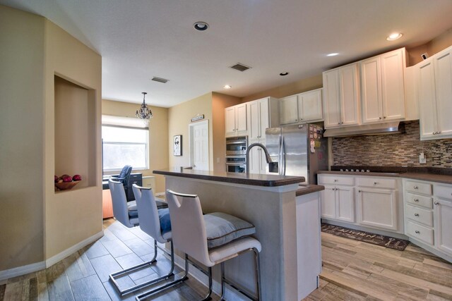 kitchen with dark countertops, an island with sink, appliances with stainless steel finishes, a kitchen bar, and pendant lighting