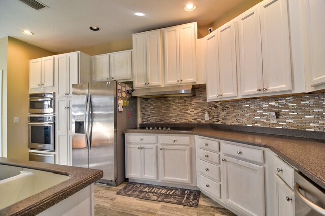 kitchen featuring stainless steel appliances, dark countertops, white cabinetry, and under cabinet range hood