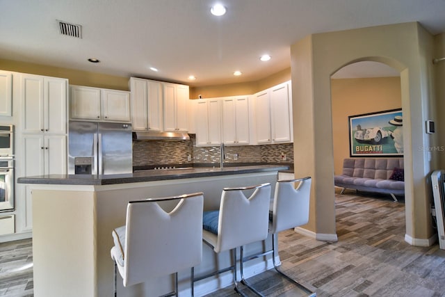 kitchen with dark countertops, a center island, under cabinet range hood, white cabinetry, and stainless steel refrigerator with ice dispenser