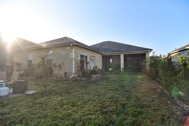 rear view of property featuring a sunroom, fence, a lawn, and stucco siding