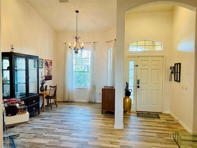 foyer entrance with baseboards, visible vents, arched walkways, wood finished floors, and an inviting chandelier