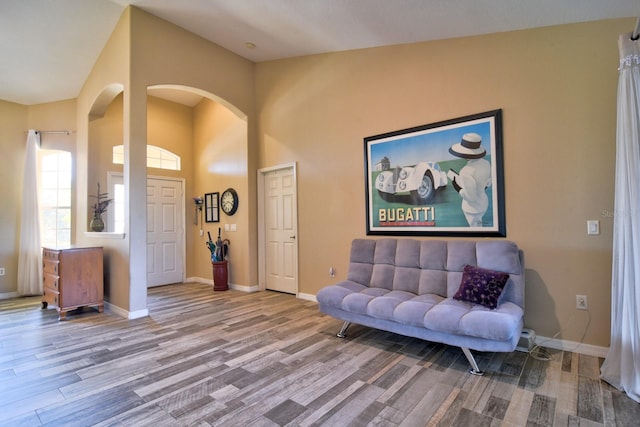 interior space with arched walkways, a high ceiling, wood finished floors, and baseboards