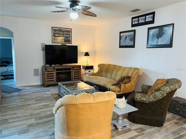 living room with arched walkways, ceiling fan, wood finished floors, visible vents, and baseboards