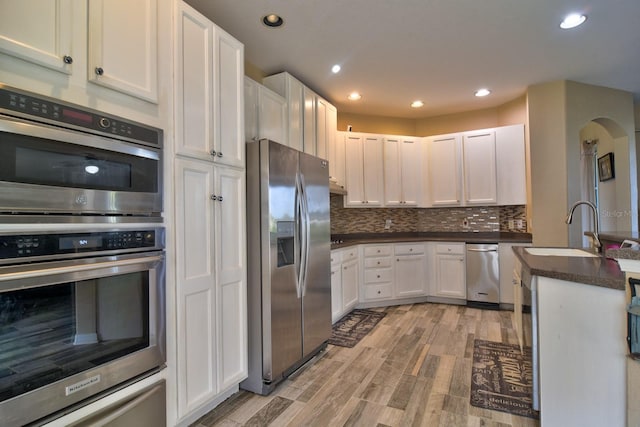 12286 23rd St E, Parrish, FL 34219 - kitchen with appliances with stainless steel finishes, arched walkways, dark countertops, white cabinets, and light wood finished floors