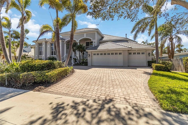 mediterranean / spanish-style home with a garage, fence, a tile roof, decorative driveway, and stucco siding