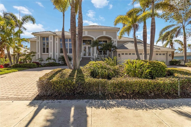 mediterranean / spanish-style house with a tile roof, an attached garage, decorative driveway, french doors, and stucco siding