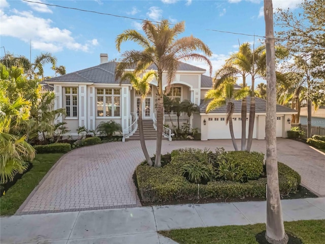 view of front of property featuring an attached garage, a tile roof, decorative driveway, stucco siding, and a chimney