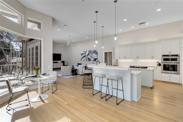 kitchen featuring an island with sink, double oven, white cabinets, and light wood-style flooring