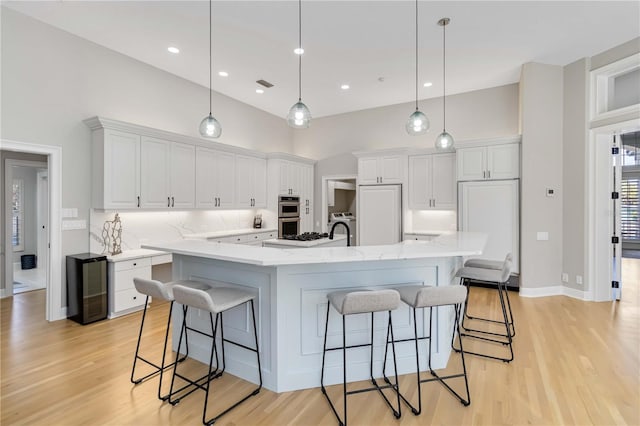 kitchen featuring stainless steel double oven, beverage cooler, white cabinetry, and a kitchen bar