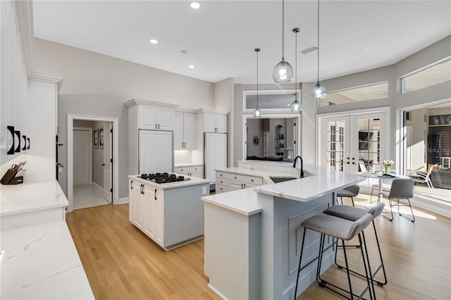 kitchen featuring french doors, a spacious island, black gas cooktop, a sink, and light wood-type flooring