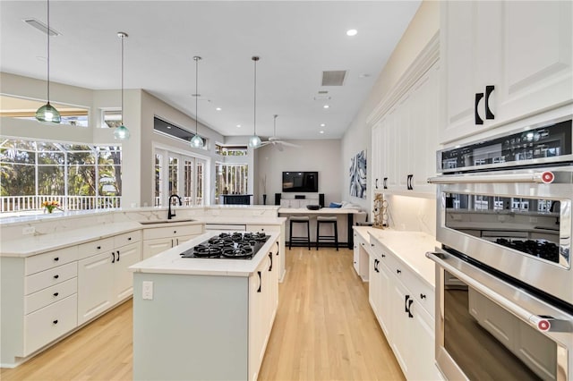 kitchen with black gas cooktop, stainless steel double oven, a sink, light wood-style floors, and a large island with sink