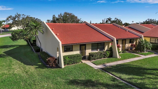 view of front facade with a front yard, a tile roof, and stucco siding