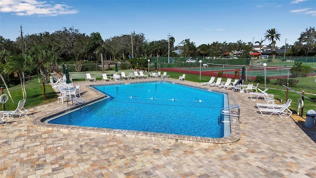 community pool featuring a tennis court, a patio area, and fence