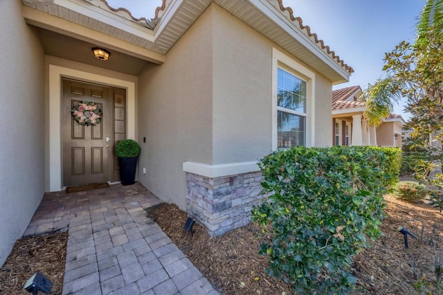 property entrance featuring stone siding, a tile roof, and stucco siding