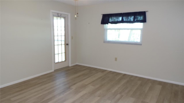 empty room featuring a wealth of natural light, baseboards, and wood finished floors