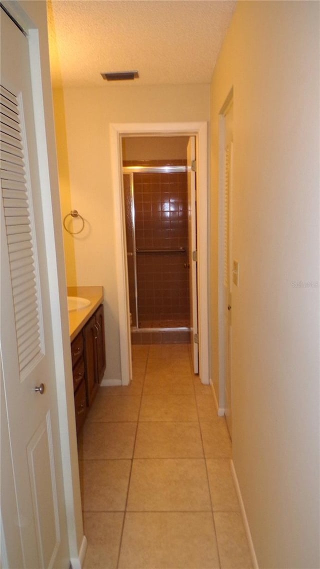 hall with visible vents, baseboards, a textured ceiling, and light tile patterned flooring