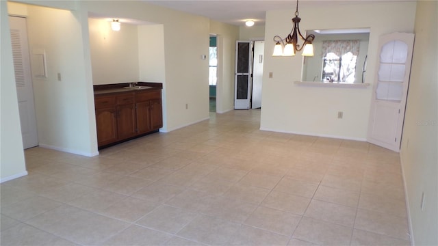 empty room featuring a sink, baseboards, an inviting chandelier, and light tile patterned floors