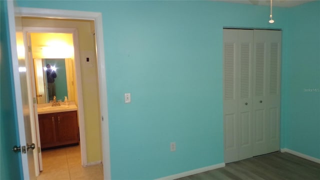 unfurnished bedroom featuring light tile patterned floors, baseboards, a closet, and a sink