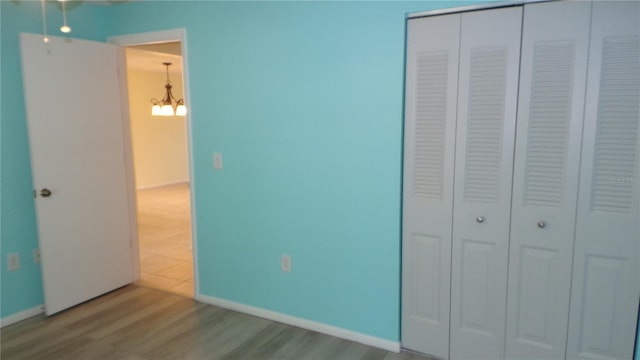 unfurnished bedroom featuring a closet, a notable chandelier, baseboards, and wood finished floors