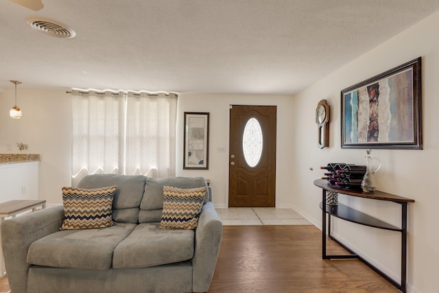 living area with a textured ceiling, wood finished floors, visible vents, and baseboards