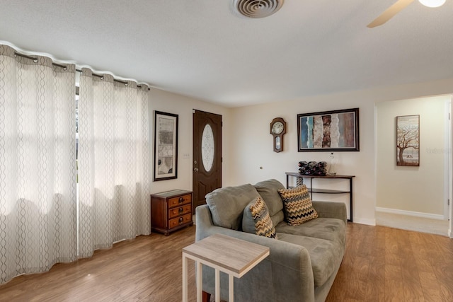 living room featuring baseboards, a ceiling fan, visible vents, and light wood-style floors