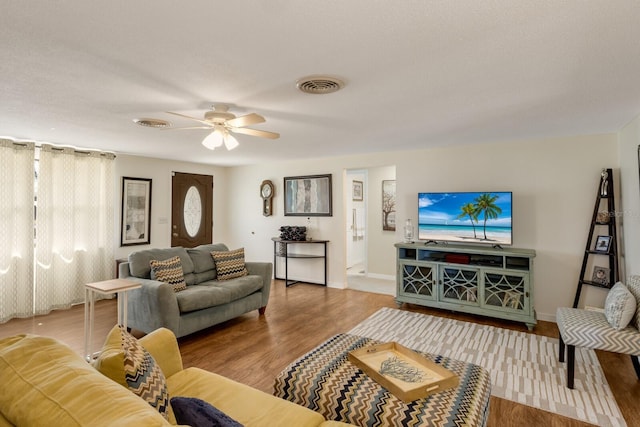 living room featuring a ceiling fan, visible vents, baseboards, and wood finished floors