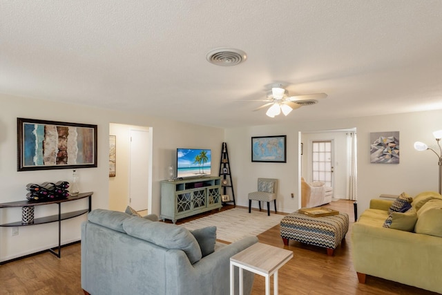 living area with a ceiling fan, a textured ceiling, visible vents, and wood finished floors