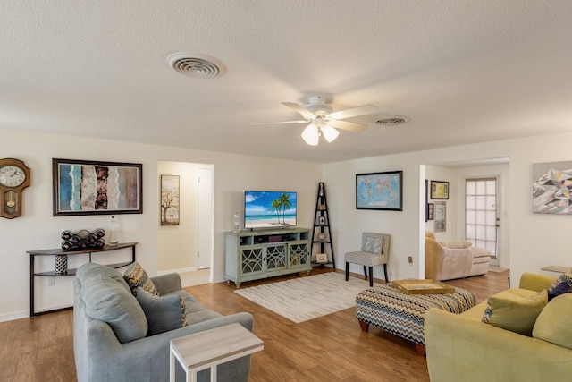 living room with a textured ceiling, wood finished floors, visible vents, and a ceiling fan