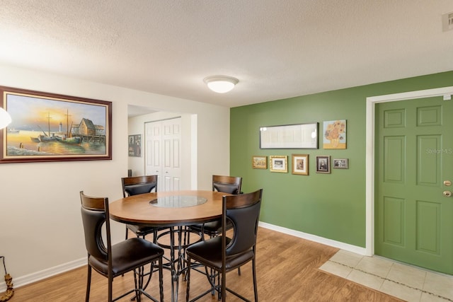 dining area featuring light wood-style floors, visible vents, a textured ceiling, and baseboards