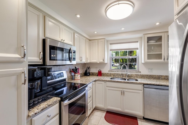 kitchen featuring light tile patterned floors, glass insert cabinets, light stone countertops, stainless steel appliances, and a sink