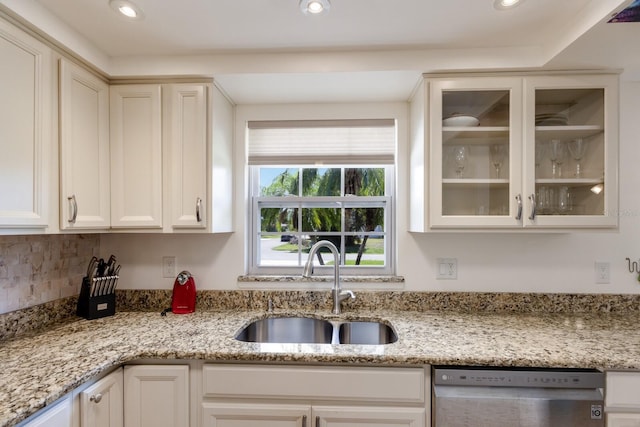 kitchen with light stone counters, stainless steel dishwasher, a sink, and glass insert cabinets