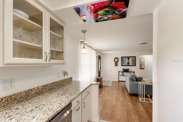 kitchen with light wood finished floors, visible vents, white cabinets, glass insert cabinets, and light stone countertops