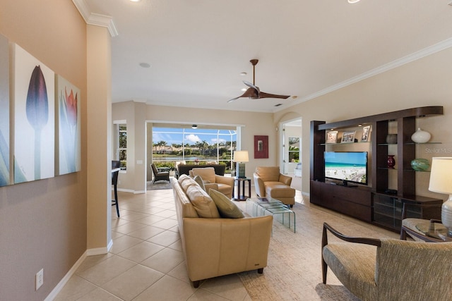 living area featuring arched walkways, light tile patterned floors, ornamental molding, ceiling fan, and baseboards