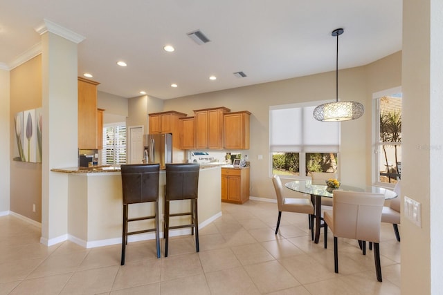 kitchen featuring recessed lighting, visible vents, baseboards, stainless steel fridge, and a kitchen bar