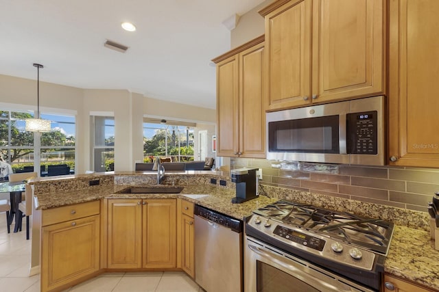 kitchen with light stone counters, a peninsula, a sink, appliances with stainless steel finishes, and backsplash