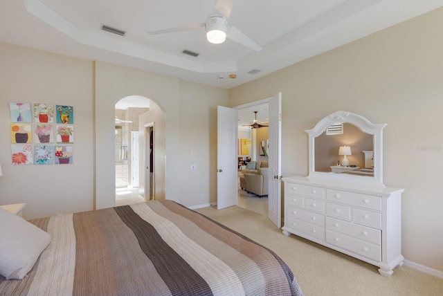 bedroom featuring light carpet, visible vents, a raised ceiling, and arched walkways