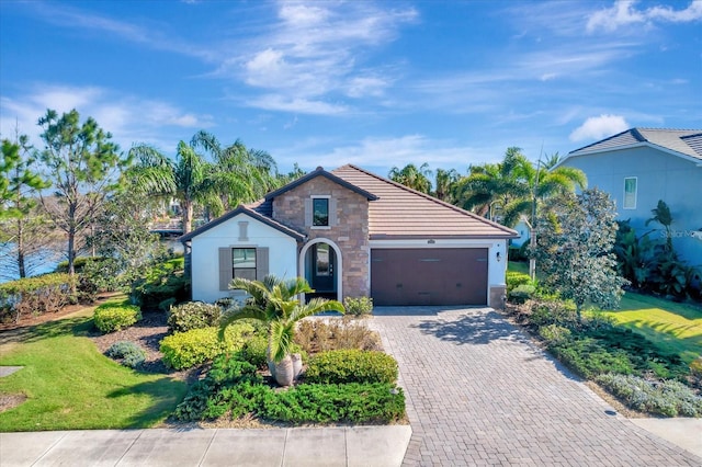 view of front of home featuring a garage, stone siding, decorative driveway, a front yard, and stucco siding